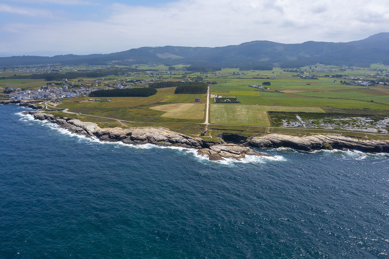 Vista panorámica. A la izquierda el pueblo con el puerto, en la parte central en el borde del mar, una de las cetáreas y en esa misma línea unos pocos metros al interior se ve el laberinto. Finalmente a la derecha el humedal, con multitud de aves.